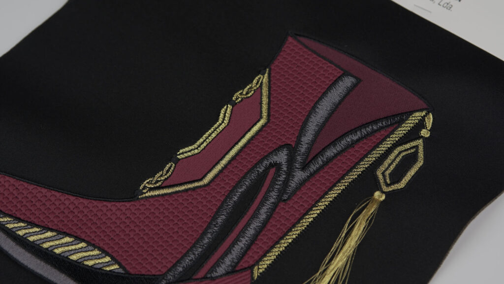 detalhe de bordado matizado com efeito que forma uma bota bordeaux com apontamentos de preto e dourado