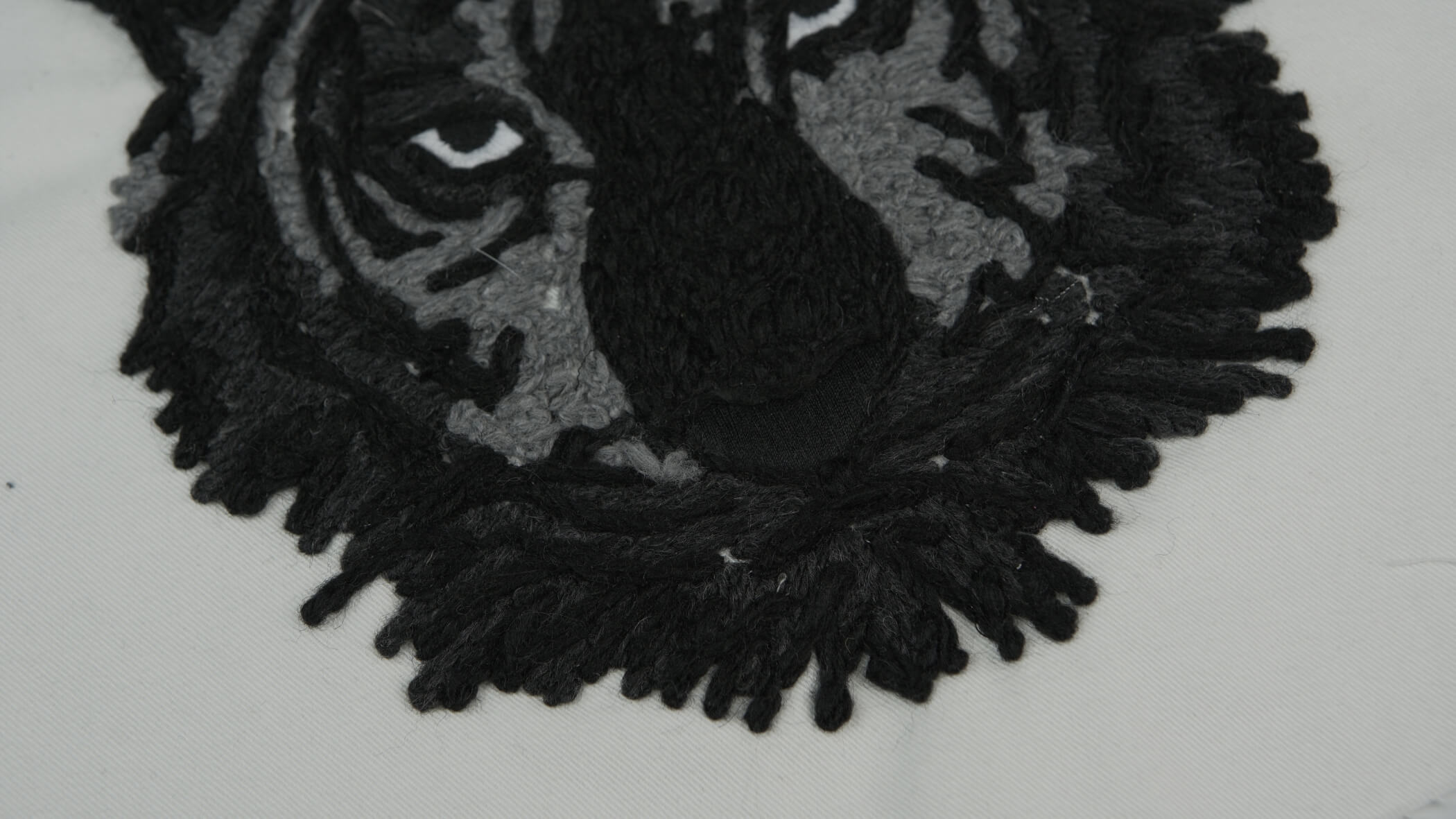 Bordado com cordão de cor preta e cinza formando o desenho da cara de um tigre