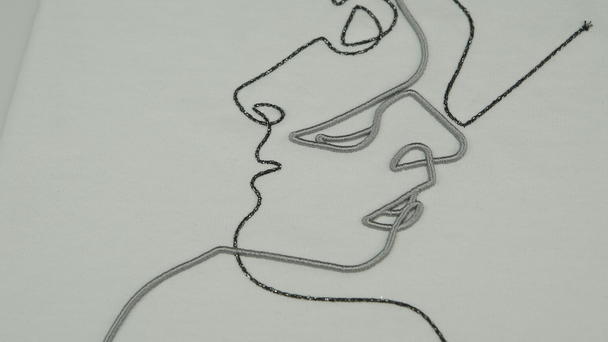 Dois rostos desenhados numa forma mais abstrata e um sob o outro, em cinzento e preto, com as técnicas de bordado com cordão e com correntes metálicas