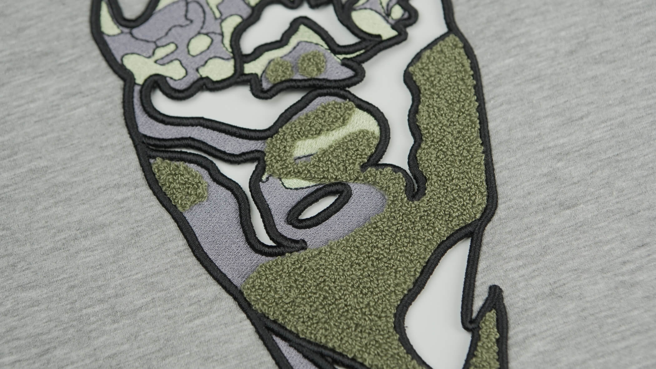 Bordado de ponto alto, formando um desenho abstrato com cores entre verde e cinzento